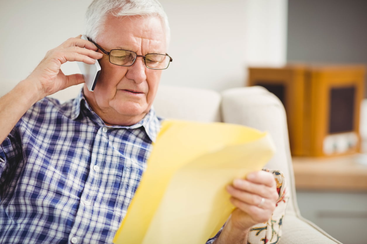 Senior man talking on mobile phone while looking at a document in living room